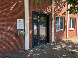 Ein rotes Backsteingebäude mit schwarzer Tür und weißen Fensterrahmen, steht an einer mit Ziegeln gepflasterten Straße. An der Wand prangt ein Kolping-Logo.