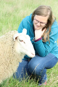 Eine junge Frau und ein Schaf sind zusammen auf einer Wiese.