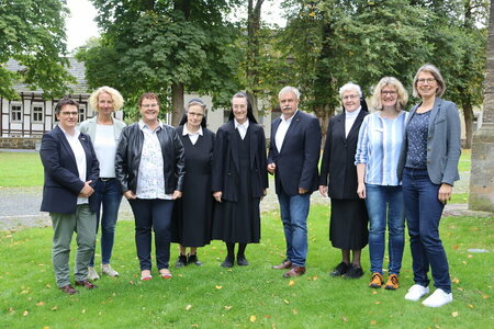 Neun Personen, darunter drei Nonnen, stehen anlässlich der Trägerübergabe der Kita Brede in Brakel auf dem Außengelände einer Kirche zusammen.