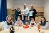 Acht Personen, darunter drei Kinder, gruppieren sich in einer Kita um einen Tisch, auf dem Experimentierequipment steht. Die drei Frauen im Hintergrund halten zwei Urkunden.
