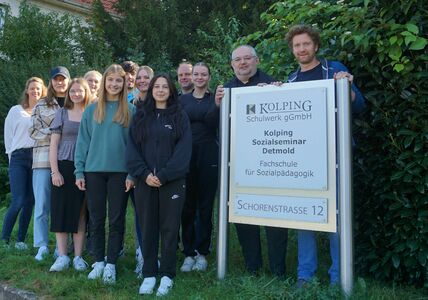 Eine Gruppe von Menschen versammelt sich anlässlich einer neuen Partnerschaft mit dem Kreissportbund Lippe um das Schulschild des Kolping-Sozialseminars Detmold.