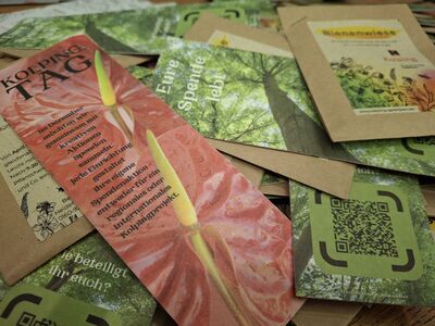 Das Lesezeichen mit angeheftetem Blumensamen macht mit einem Waldmotiv auf der Vorderseite und einem Blumenmotiv auf der Rückseite Werbung für die neue Aktion zum Kolpingtag.