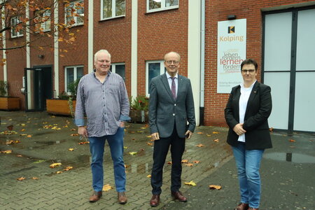 Drei Personen stehen vor dem Backsteingebäude des Kolping-Berufskollegs Gütersloh.
