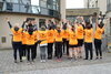 Eine Gruppe von Menschen in orangefarbenen "Kolping"-Shirts posiert anlässlich des Firmenlaufs vor dem Hotel Aspethera in Paderborn mit erhobenen Händen. Die Männer und Frauen stehen mit dem Rücken zur Kamera.