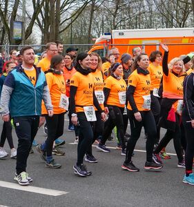 Eine Gruppe von Läufern und Läuferinnen in orangefarbenen Kolping-Shirts nimmt am Firmenlauf teil.