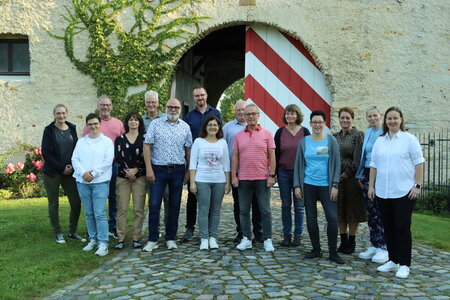 Eine Gruppe von 15 Personen versammelt sich vor einem rot-weiß gestreiften Torbogen eines Rittergut, an dem Efeu rankt.