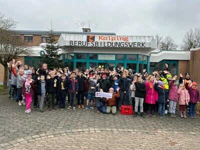 Eine Gruppe von Kindern und Jugendlichen steht anlässlich eines Spendenlaufs vor ihrer Schule und winkt in die Kamera.