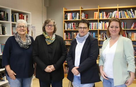 Vier Frauen stehen vor den Regalen einer Schulbibliothek anlässlich eines Besuchs aus der Politik.