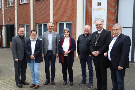 Sieben Personen, darunter ein Priester, versammeln sich vor dem Schulgebäude des Kolping-Berufskollegs Gütersloh anlässlich der Visitation des Weihbischofs.